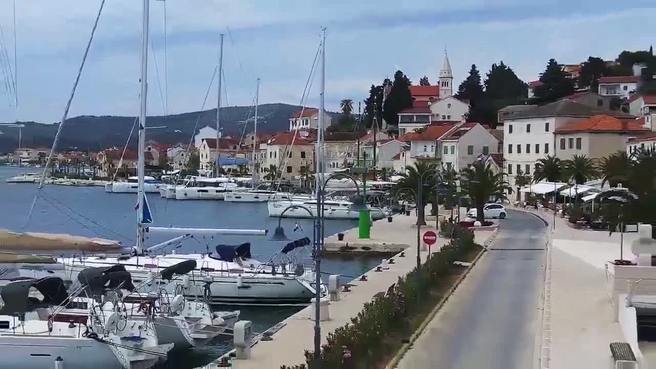 A harbor filled with sailboats is situated next to a waterfront town under a partly cloudy sky.