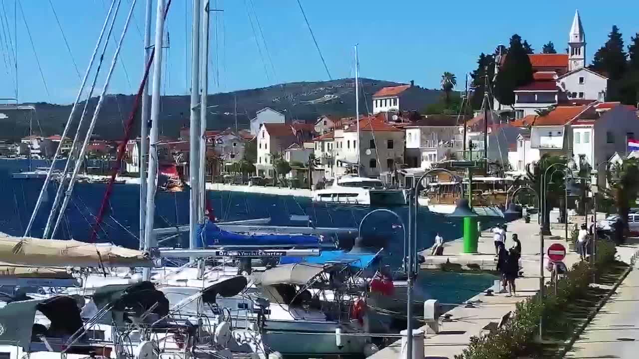 A marina filled with sailboats and motorboats is situated in front of a waterfront town on a sunny day.