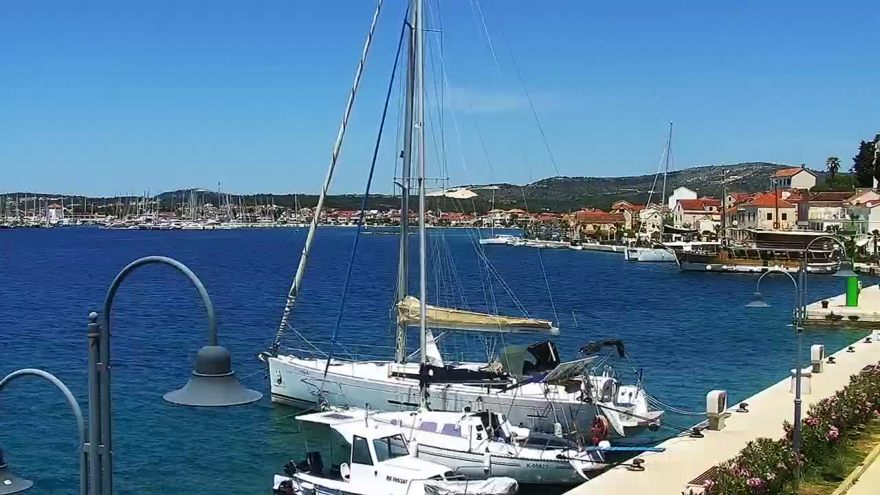 A marina filled with sailboats and motorboats on a sunny day, with a town visible in the background.