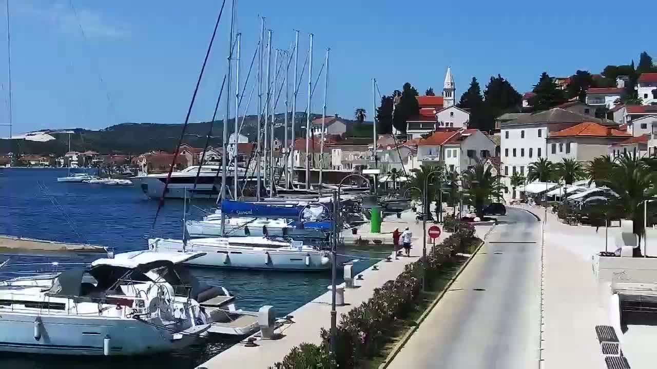 A marina filled with sailboats is situated next to a town of white and red buildings under a clear blue sky.