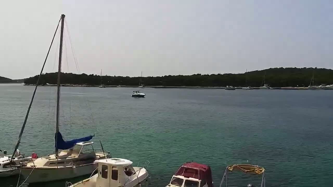 Several boats are moored in a calm, teal-colored bay, with a line of dark green, forested land in the background under a bright, hazy sky.