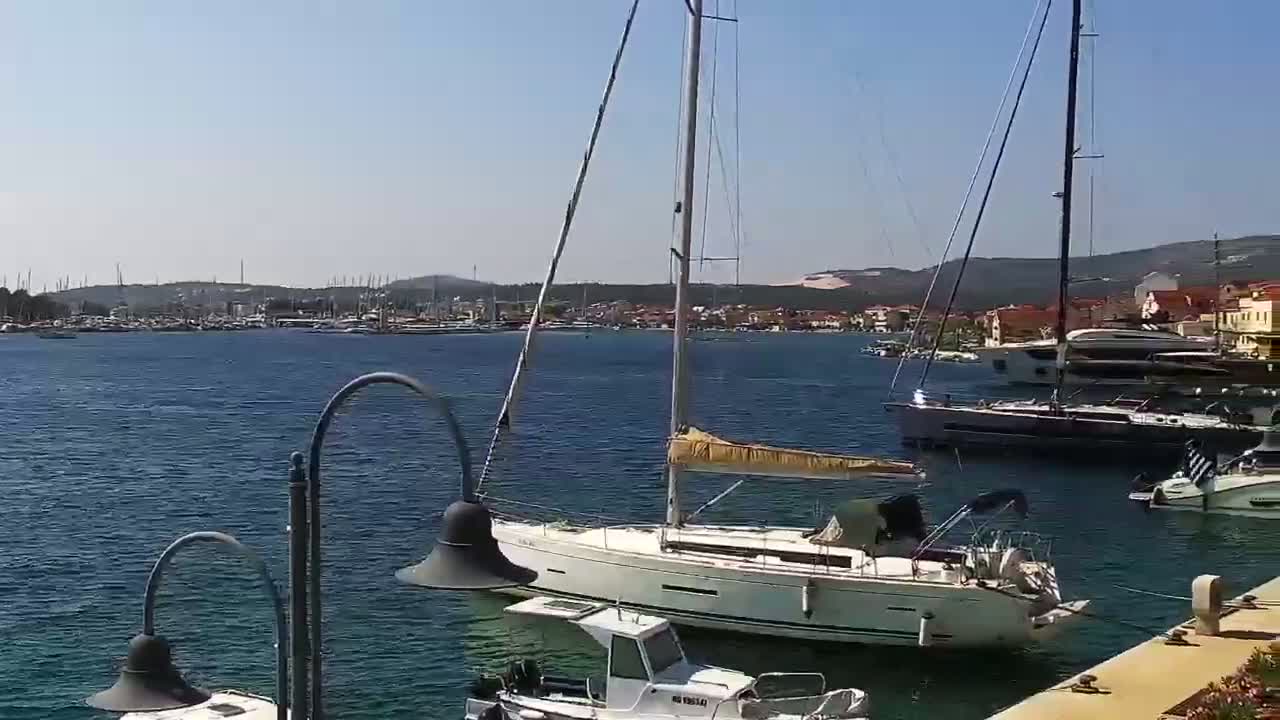 A marina filled with sailboats and motorboats on a sunny day, with a town visible in the background.