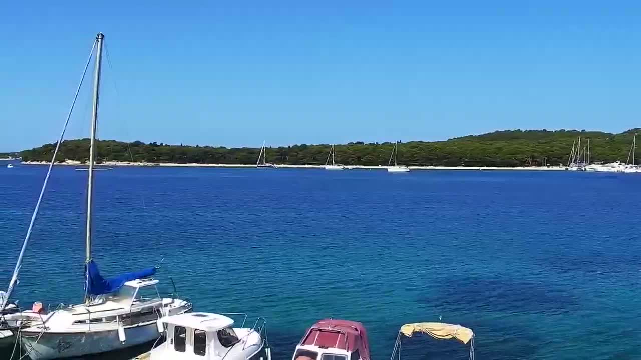 Several boats are moored in a calm, clear blue sea under a bright sunny sky, with a verdant island visible in the background.