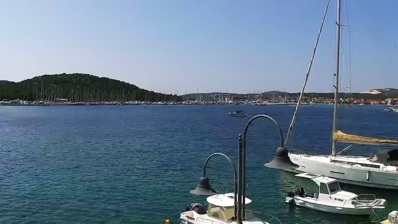 A calm, sunny day shows a harbor filled with sailboats and yachts, with a few smaller motorboats in the foreground.