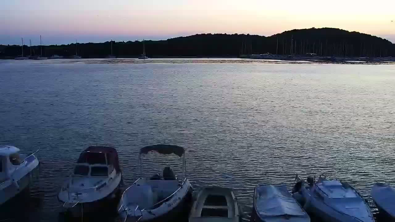 A calm, sunny day shows a harbor filled with sailboats and yachts, with a few smaller motorboats in the foreground.