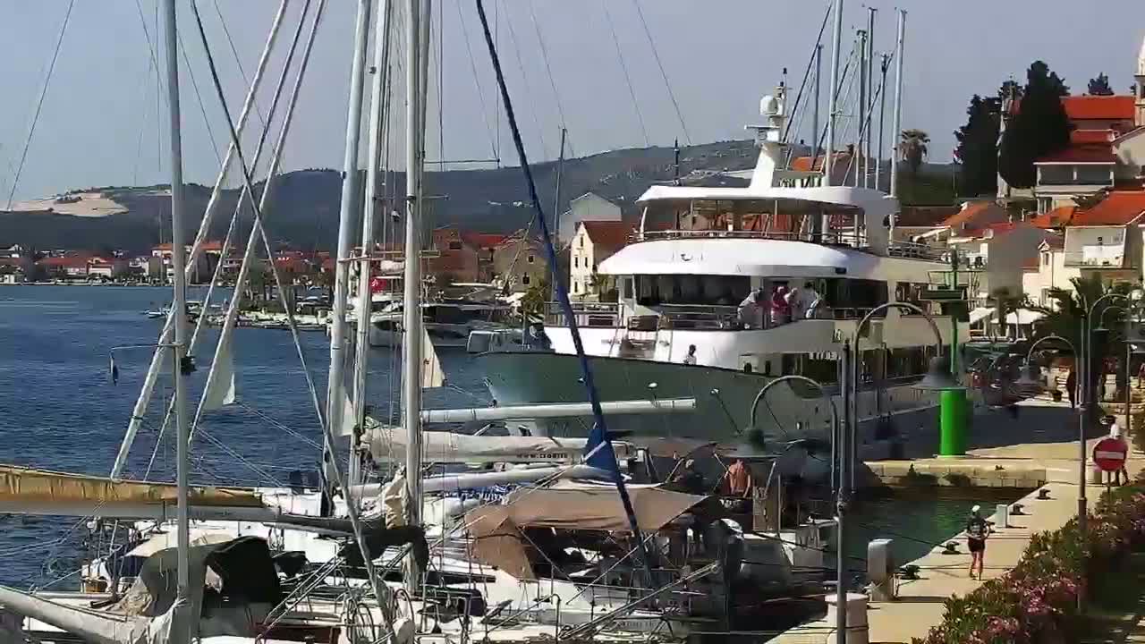 A large motor yacht is docked in a marina filled with sailboats on a sunny day.