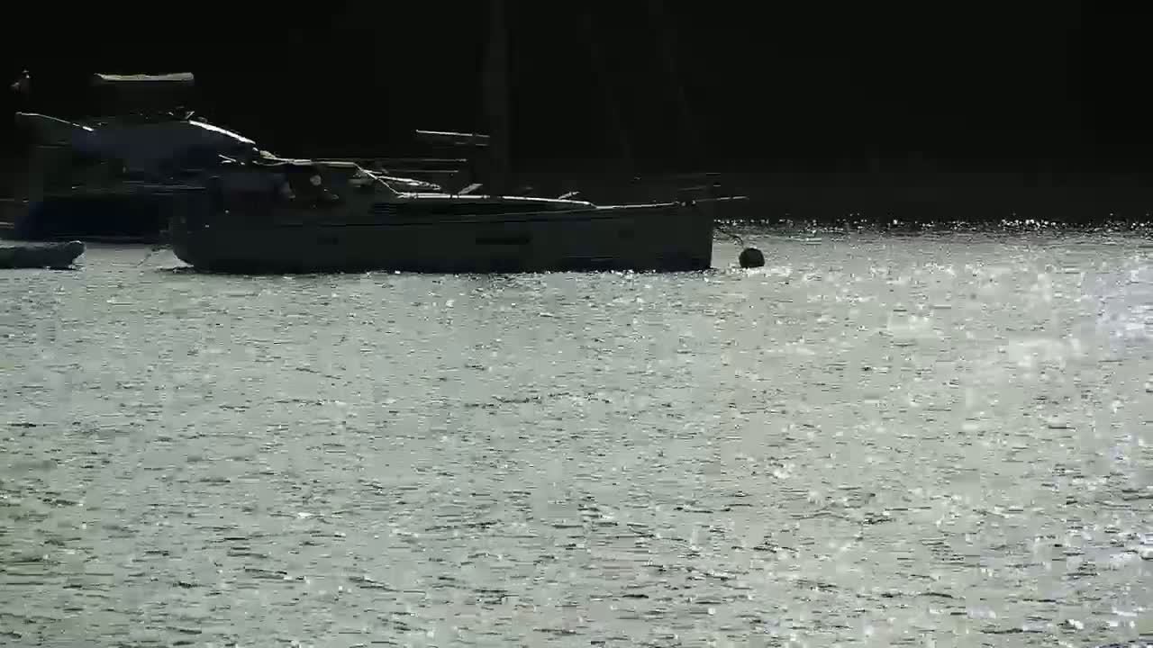 Two boats are moored in calm, glistening water.