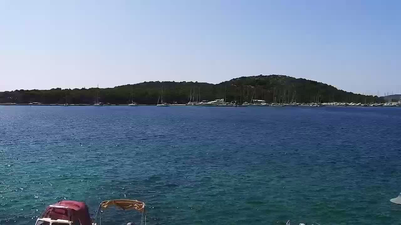 A calm, clear day reveals a body of teal water with numerous boats docked at a tree-lined shore.