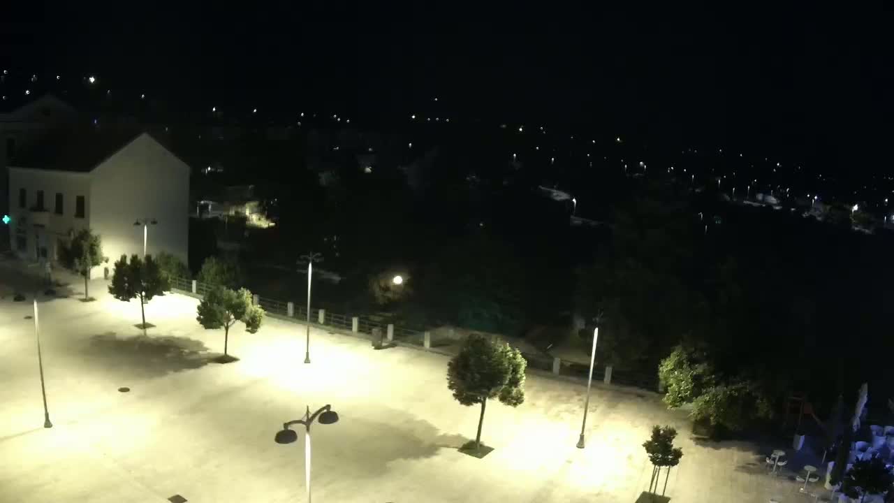 An empty, brightly lit plaza at night overlooks a dark body of water with distant lights.