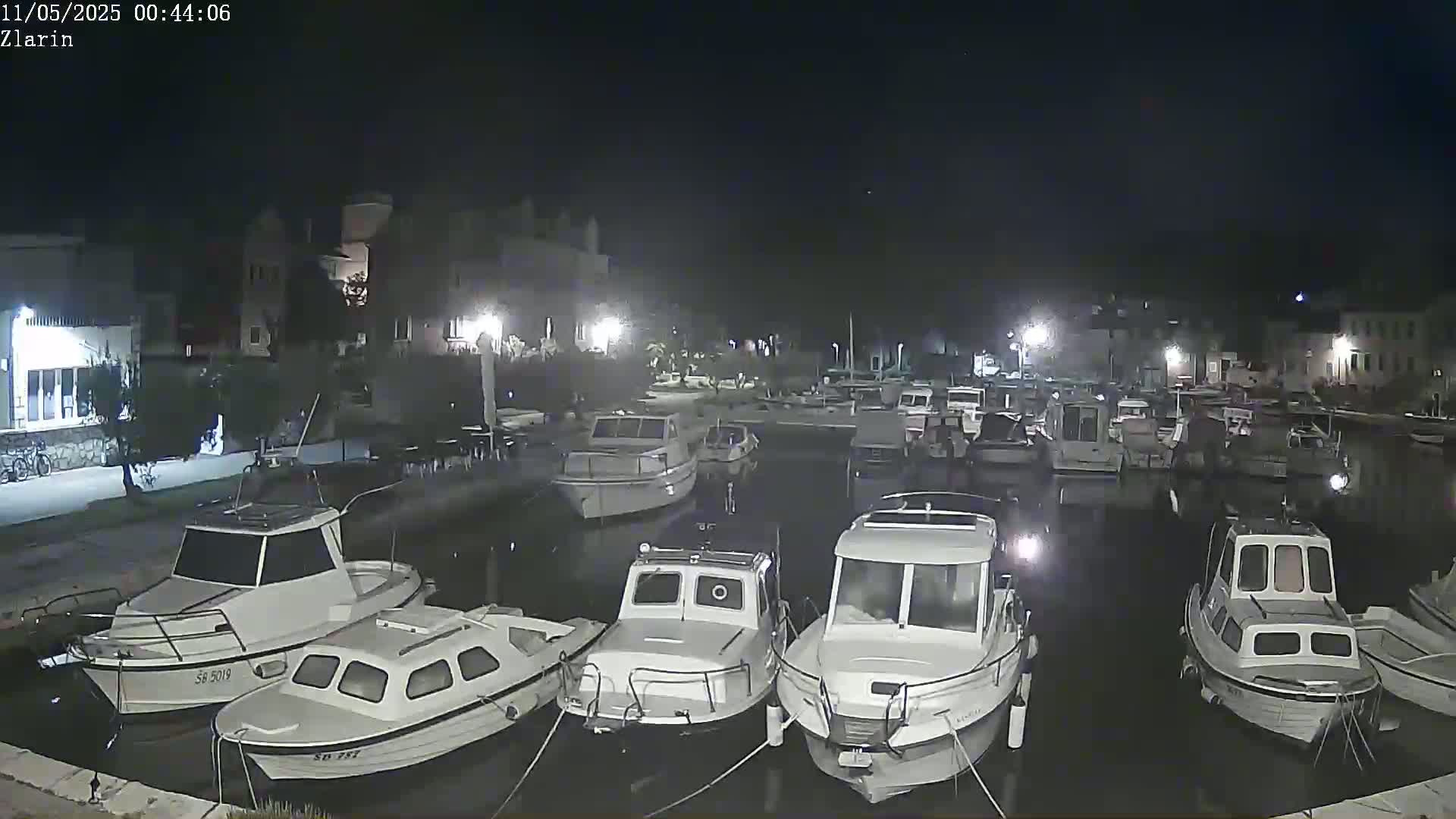 Several small motorboats are moored in a calm harbor at night, under a clear, dark sky.