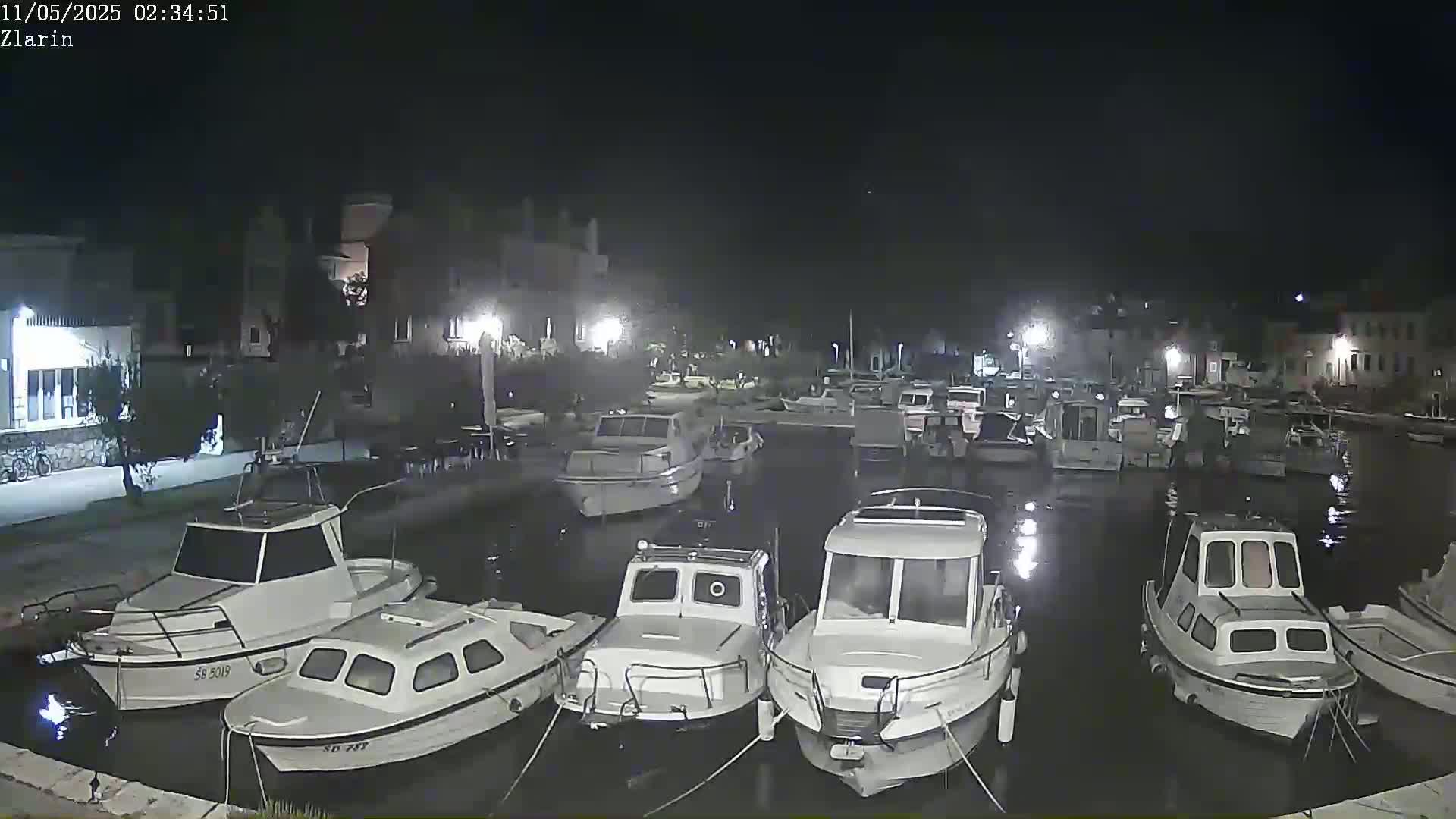Several small motorboats are moored in a calm harbor at night.