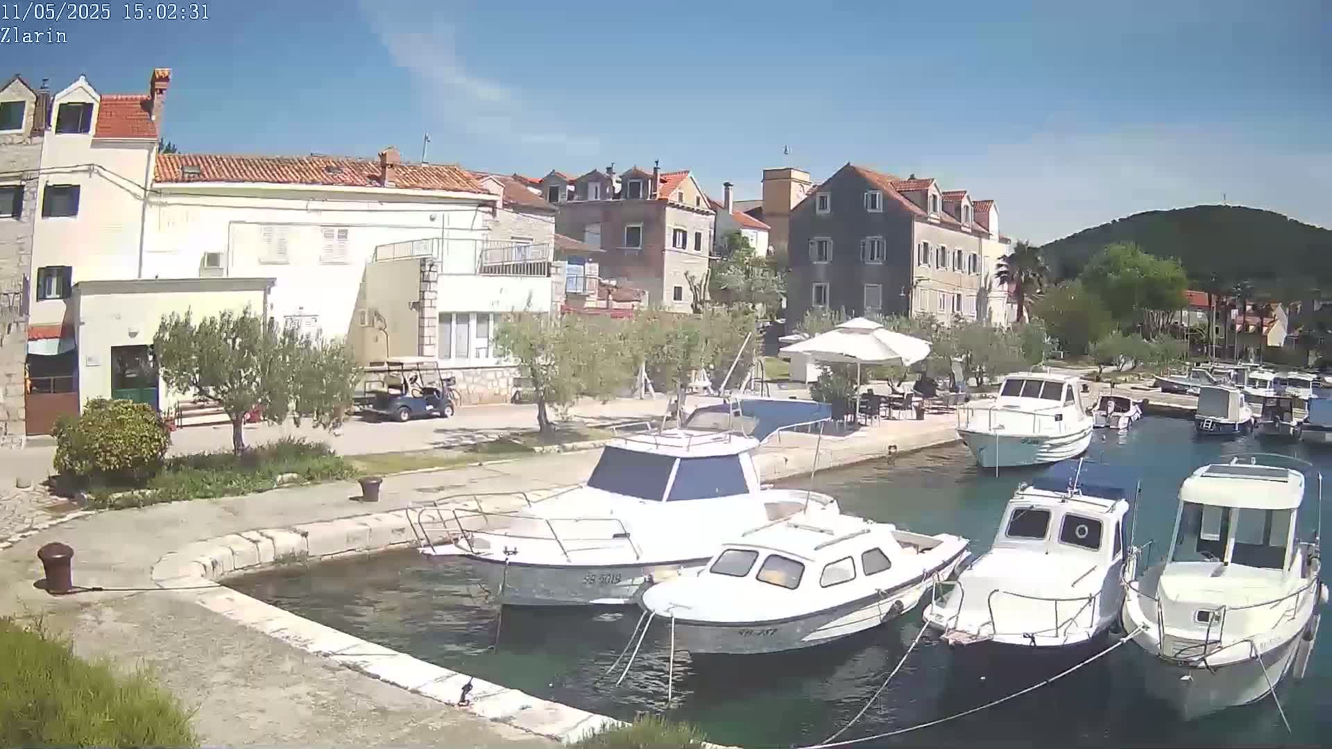 Several motorboats are moored in a calm harbor next to a waterfront village under a clear, sunny sky.