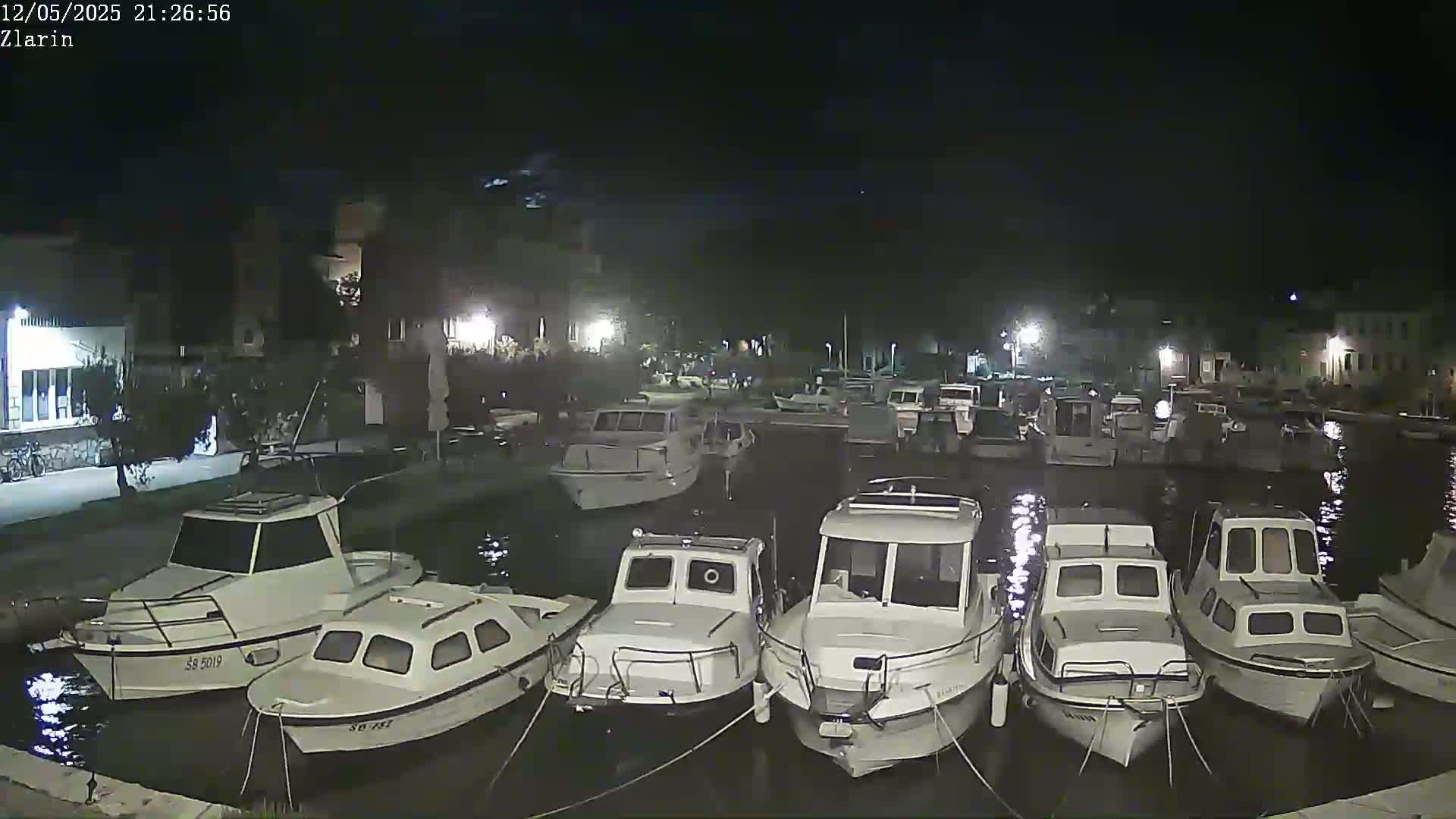 Several small white motorboats are moored in a calm harbor at night.