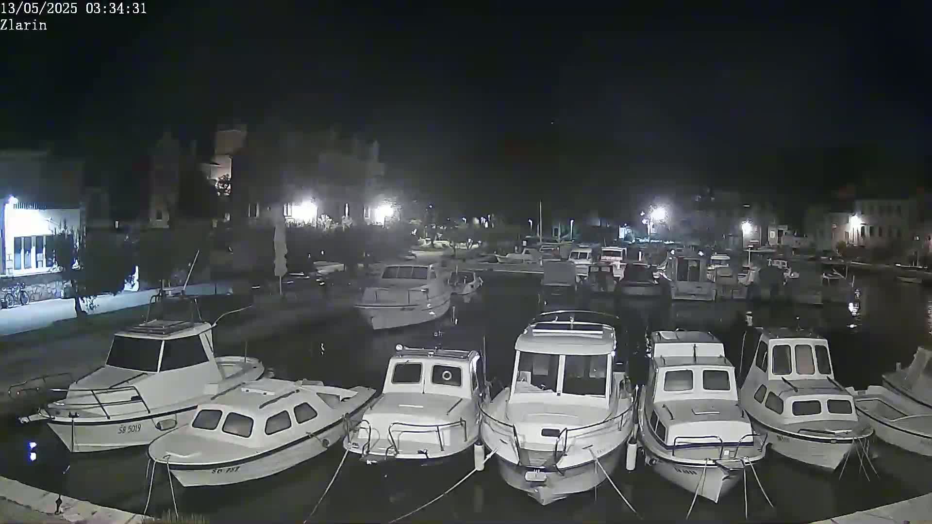 Several white motorboats are moored in a calm harbor at night.