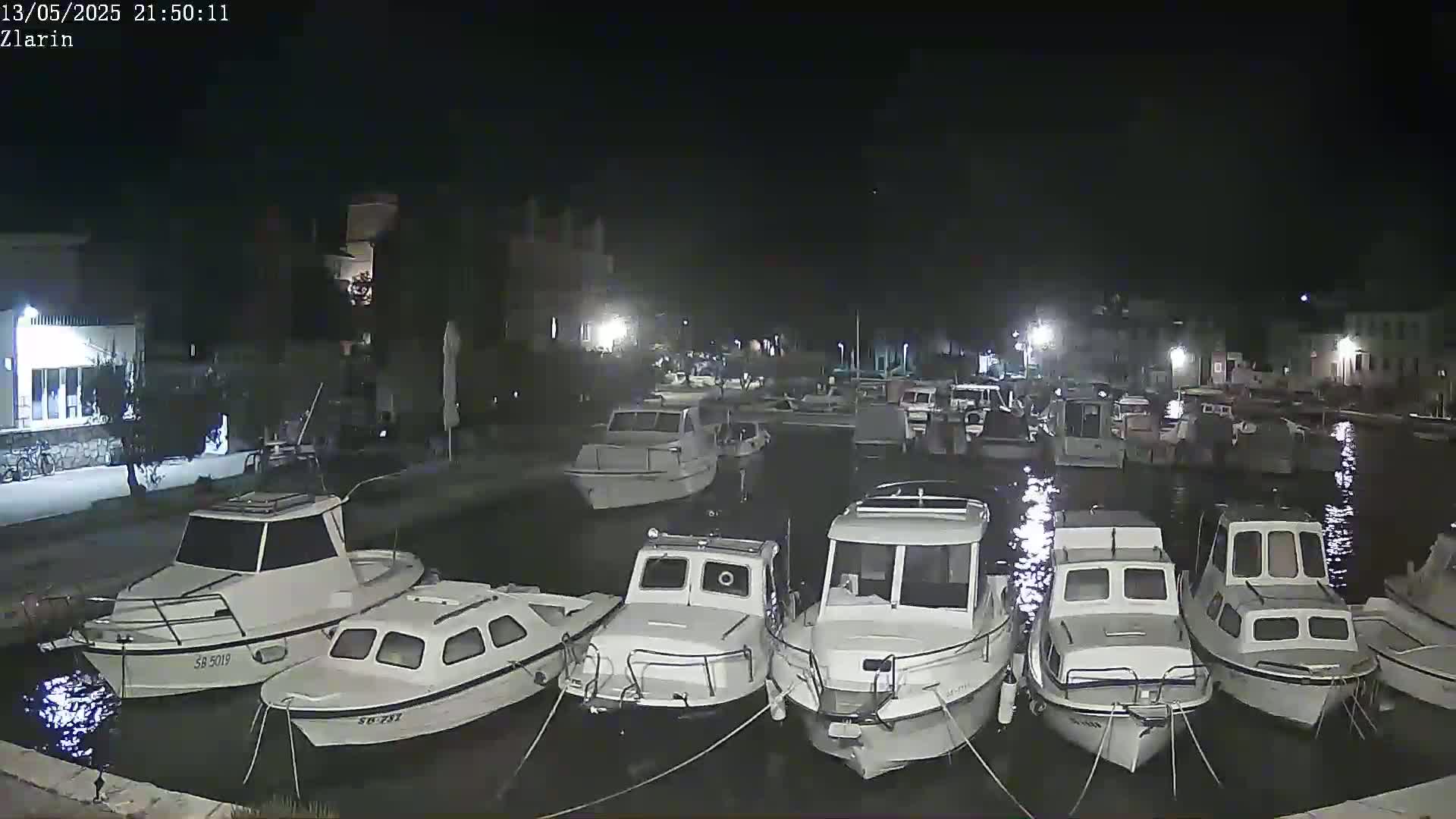A nighttime view of numerous small boats moored in a calm harbor next to a waterfront building.