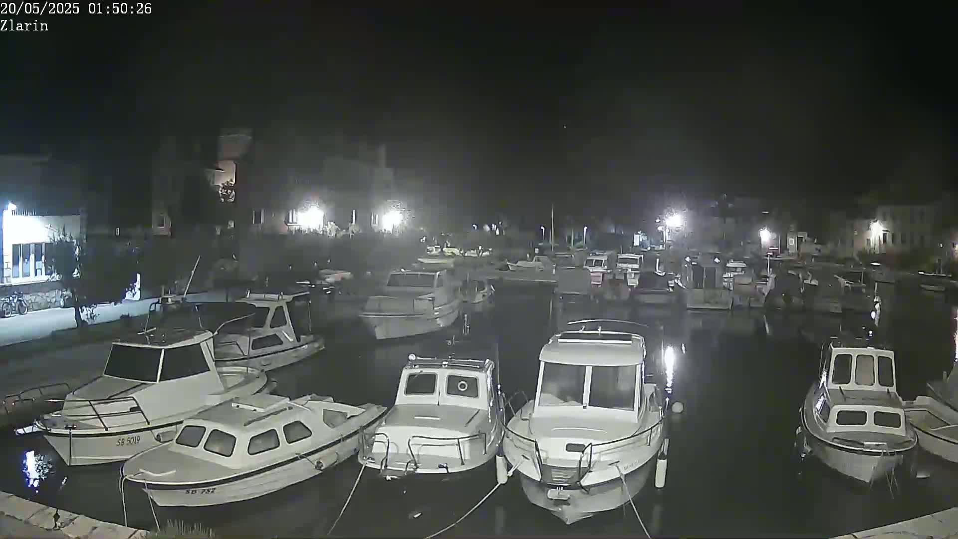 Numerous small boats are moored in a calm harbor at night under a dark sky.