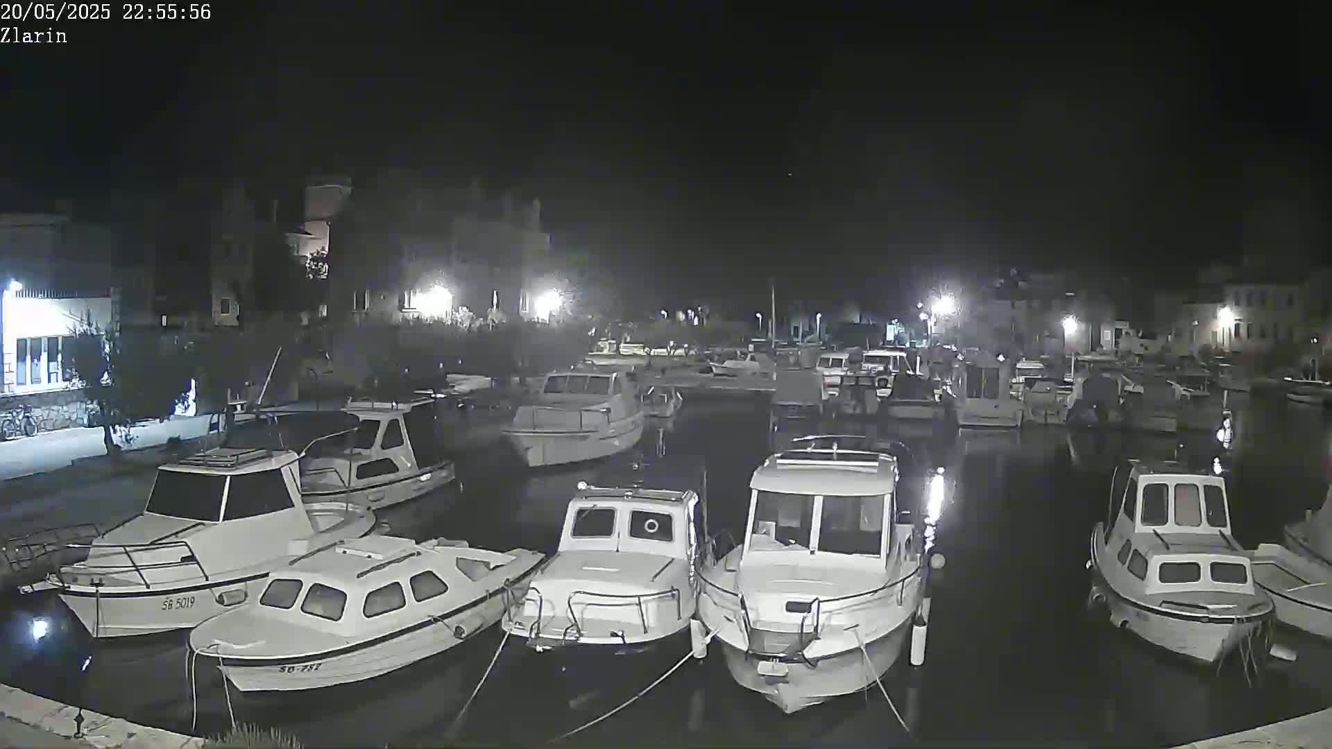 A nighttime view of a marina filled with numerous small, white motorboats moored in calm water under a dark sky.