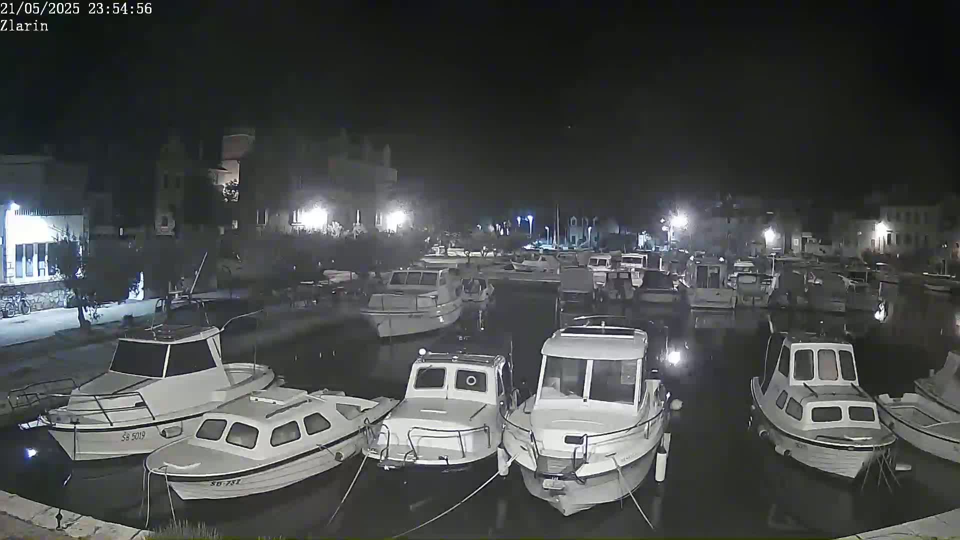 A nighttime view of a harbor filled with numerous boats moored alongside a waterfront with buildings visible in the background.