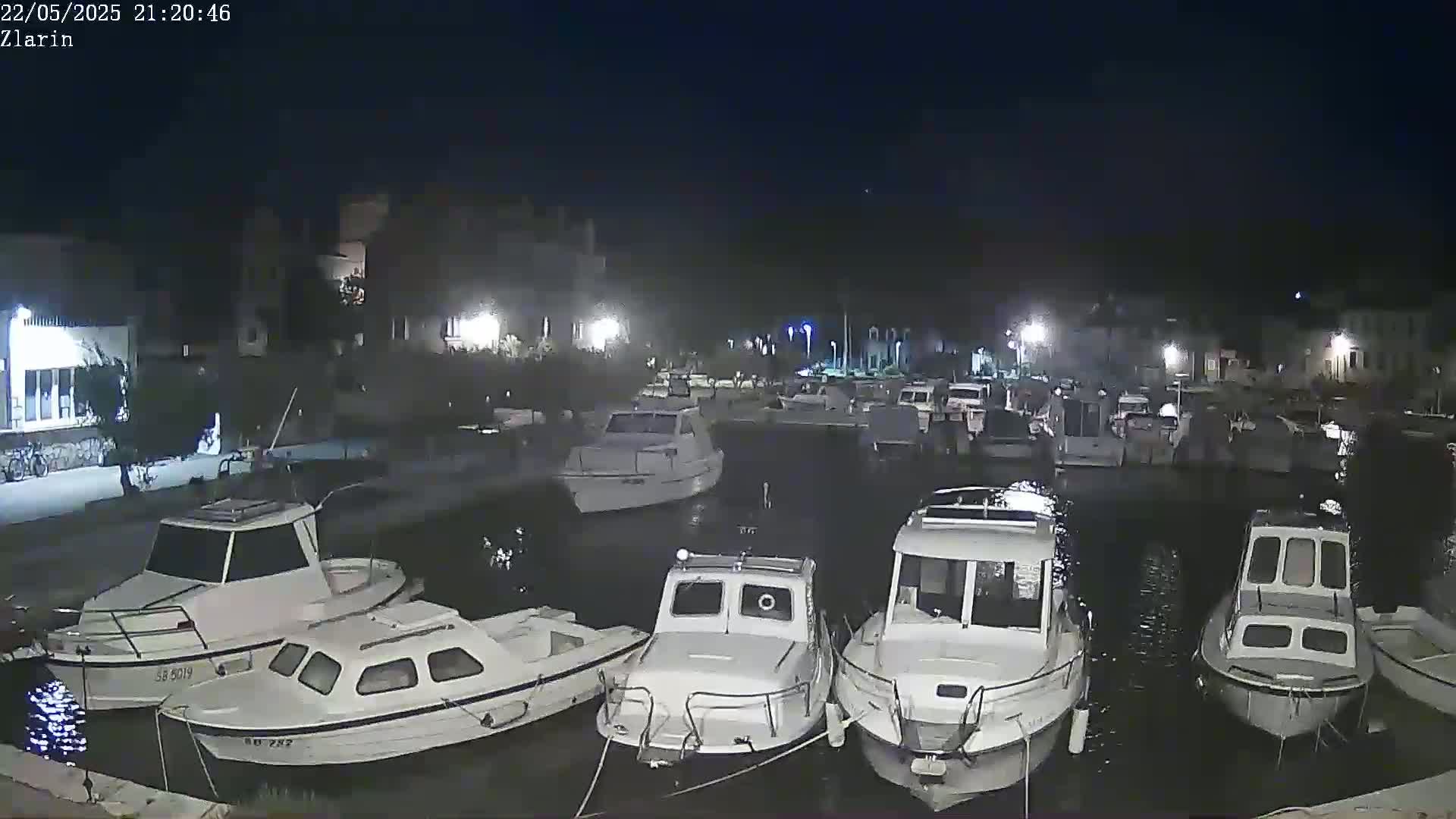 Several white motorboats are moored in a calm harbor at night.