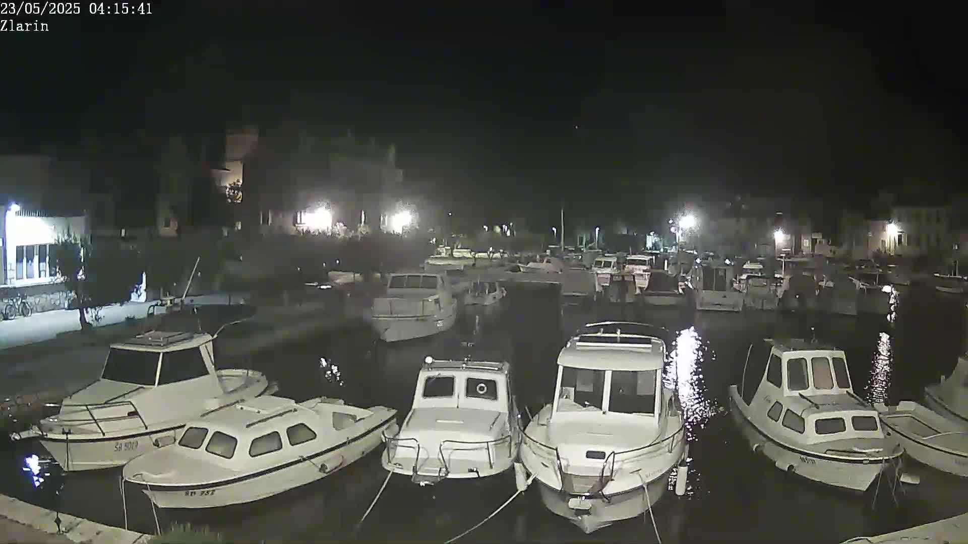 Many small white motorboats are docked in a calm harbor at night.