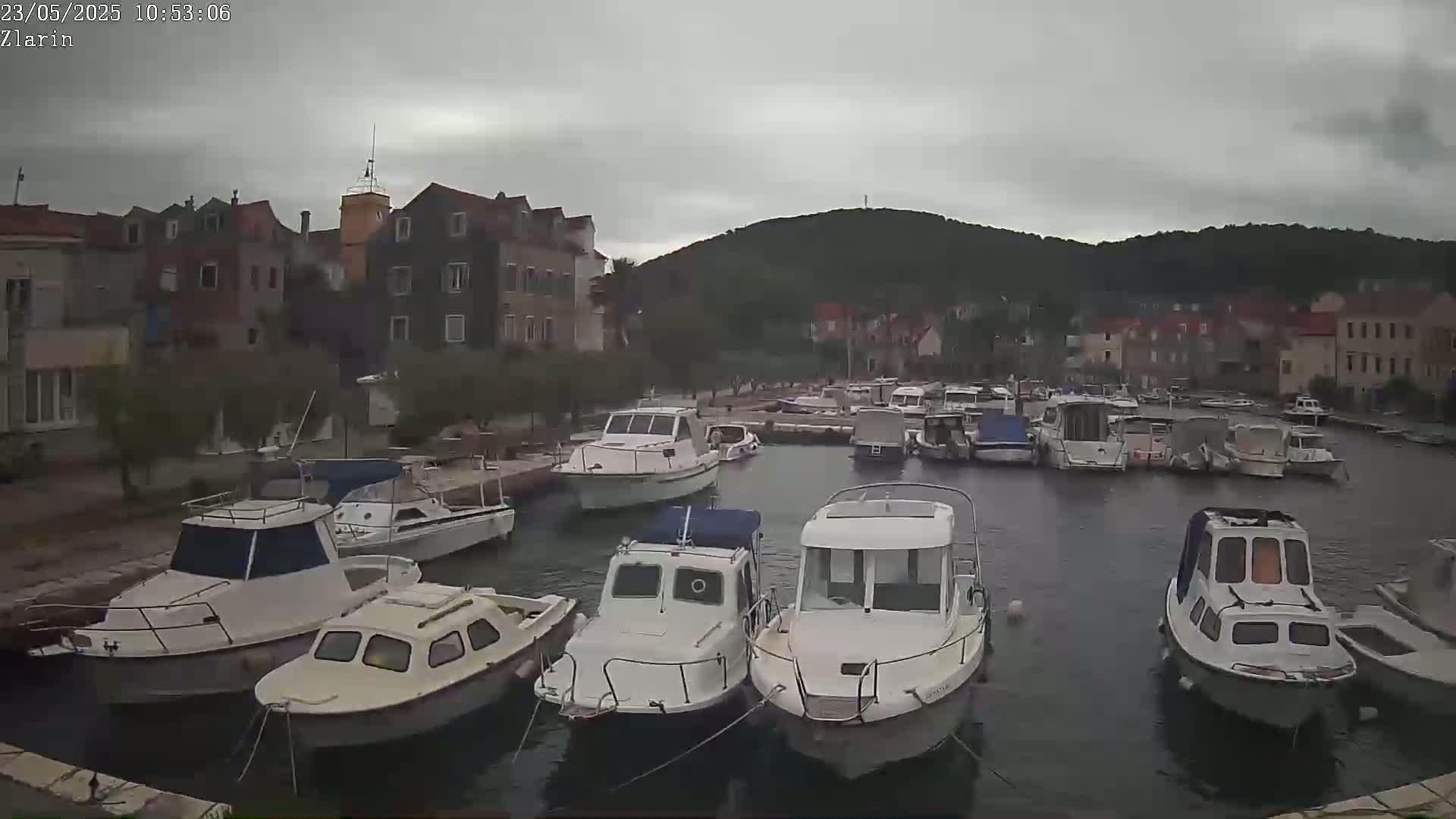 Numerous boats are moored in a calm harbor next to a small town under an overcast sky.