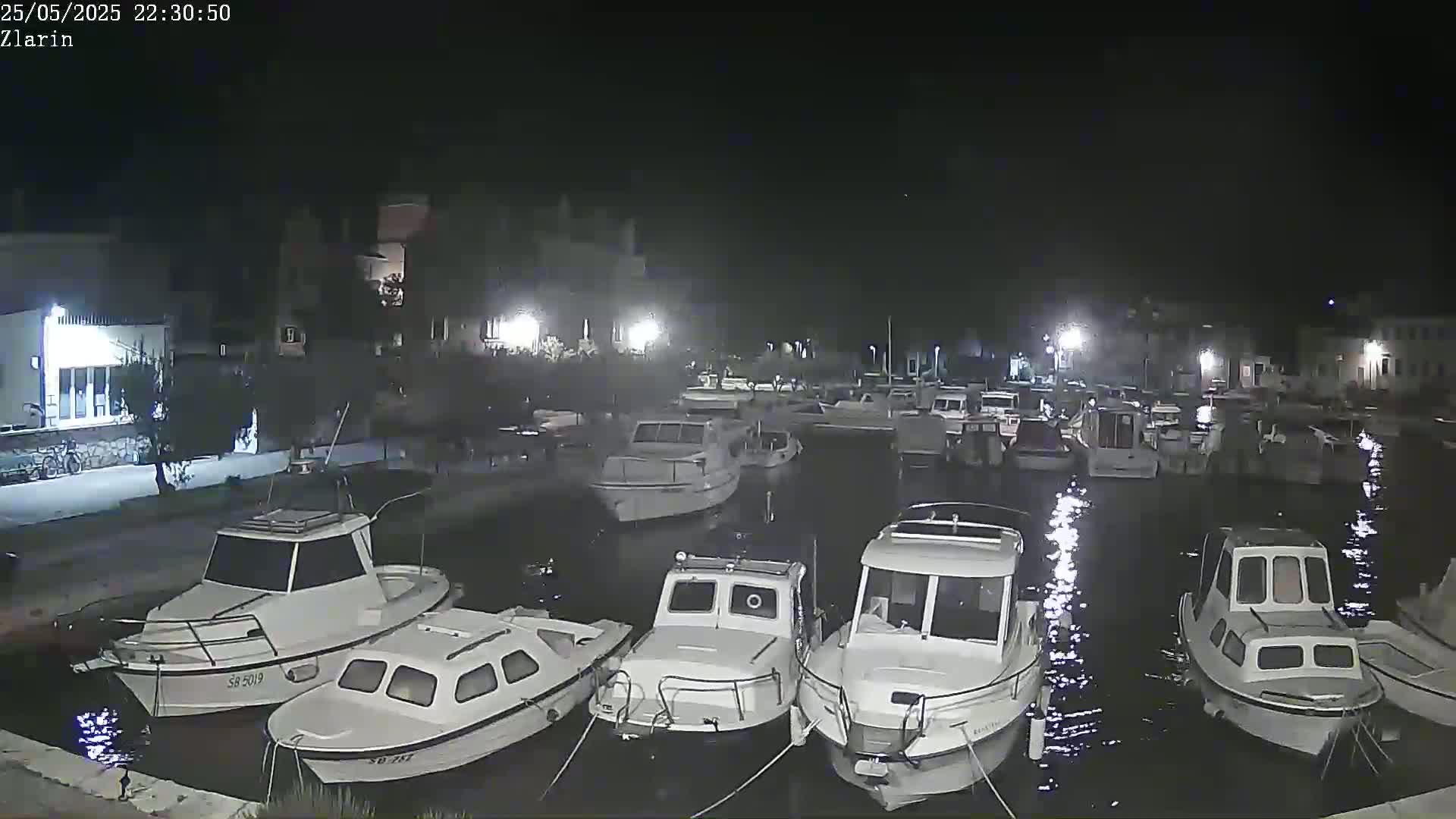 Several white motorboats are docked in a calm harbor at night.