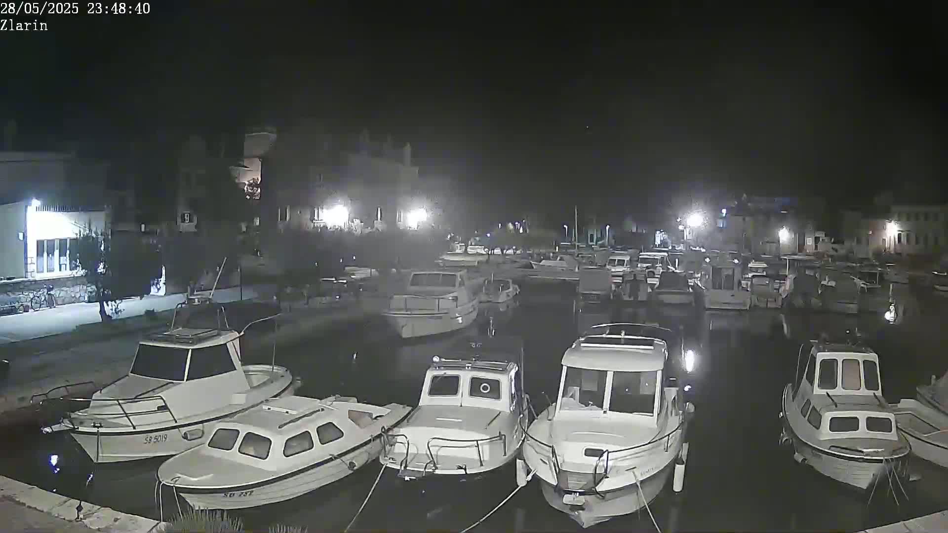 Numerous white boats are moored in a calm harbor at night under a dark, clear sky.