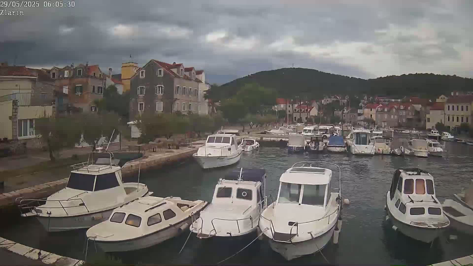 A harbor filled with numerous small motorboats is situated next to a stone village under an overcast sky.