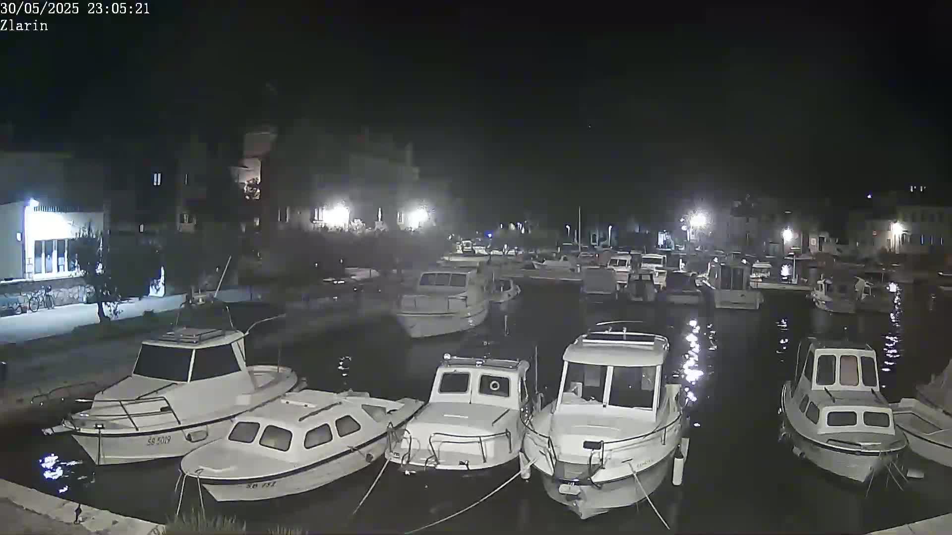 Several small motorboats are moored in a calm harbor at night under a clear, dark sky.