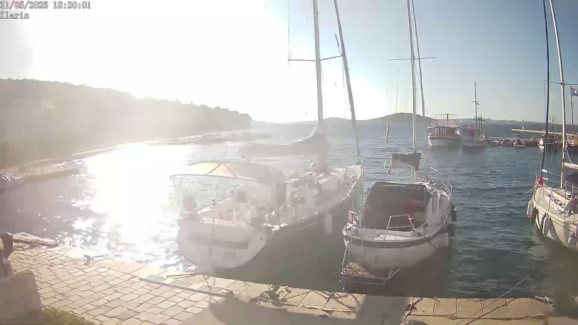 Several sailboats and motorboats are moored in a calm harbor on a sunny day.