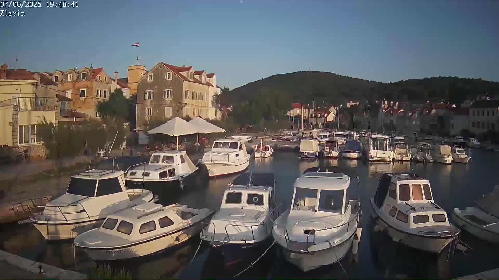 Many small white motorboats are docked in a calm harbor next to a village of stone buildings under a clear twilight sky.