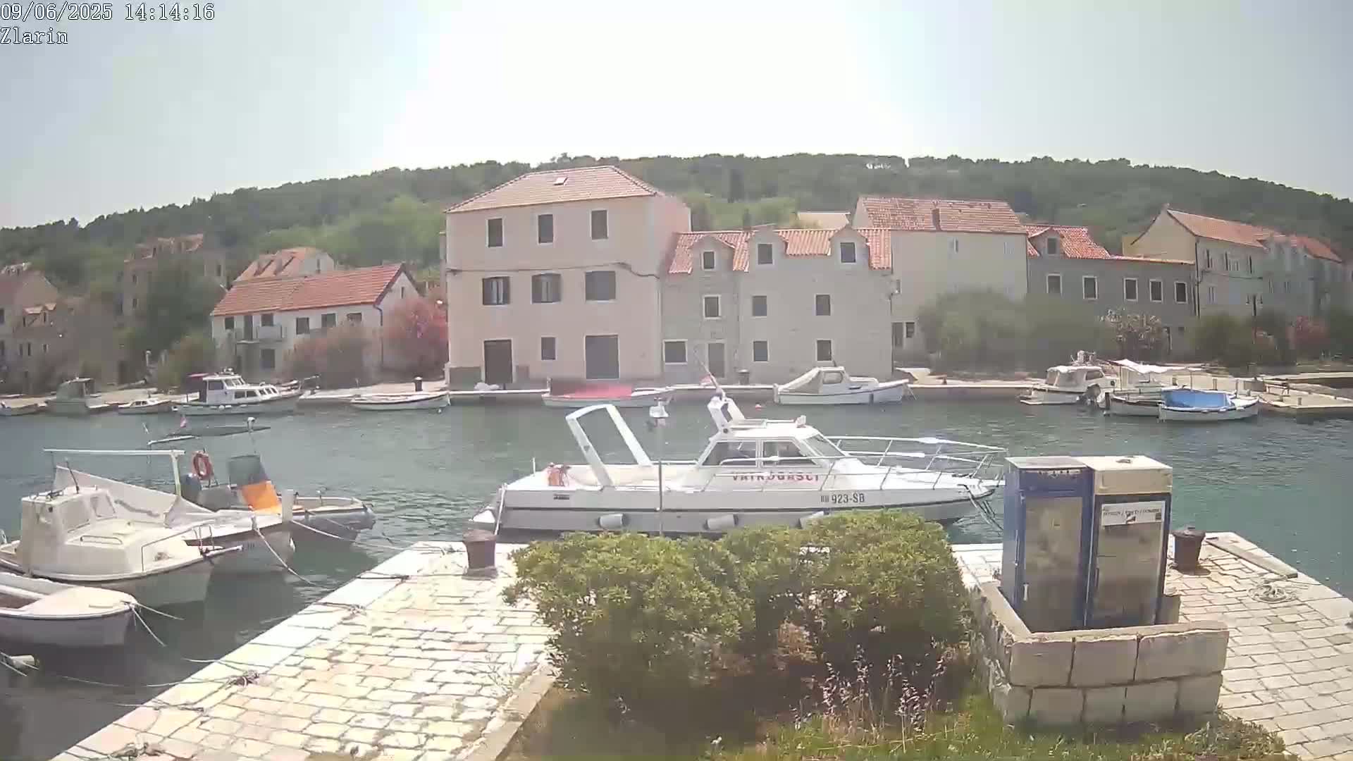 A harbor filled with several boats is situated in front of a collection of buildings on a sunny day.
