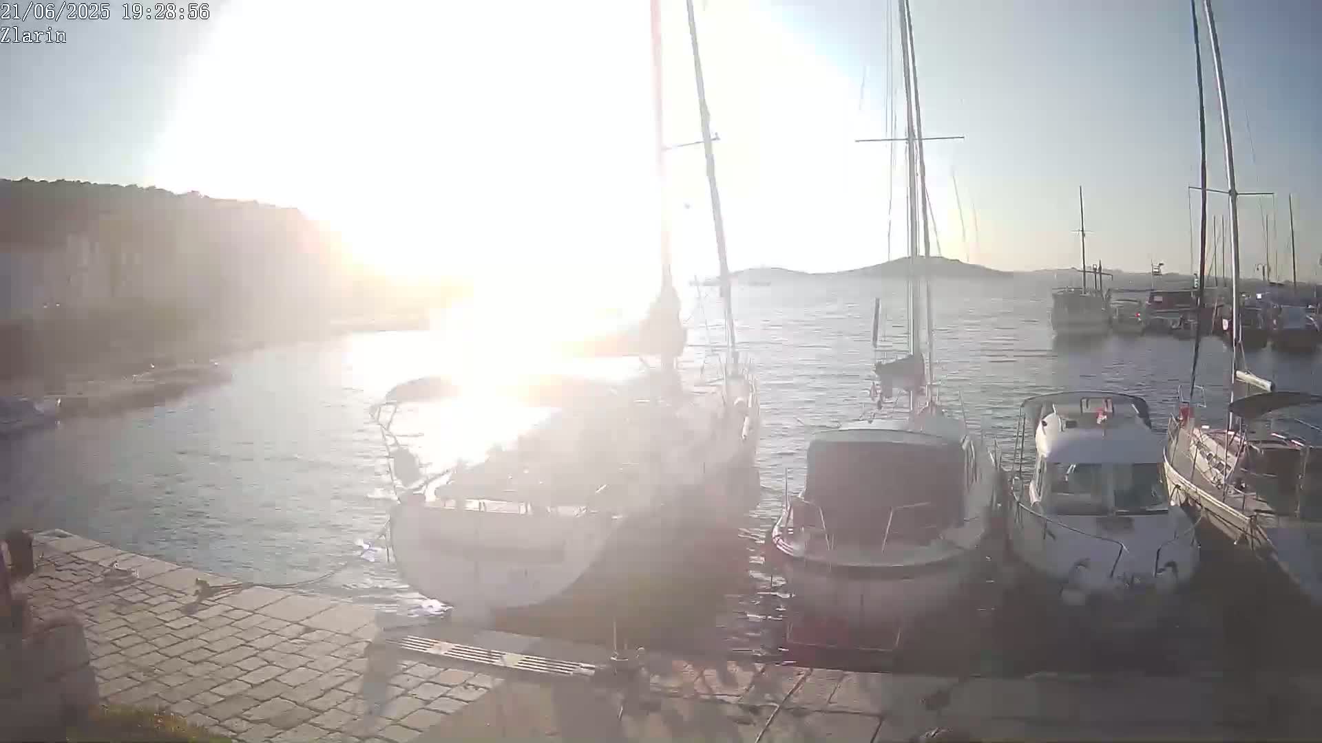 Several sailboats and motorboats are moored at a dock in calm water under a bright, sunny sky.