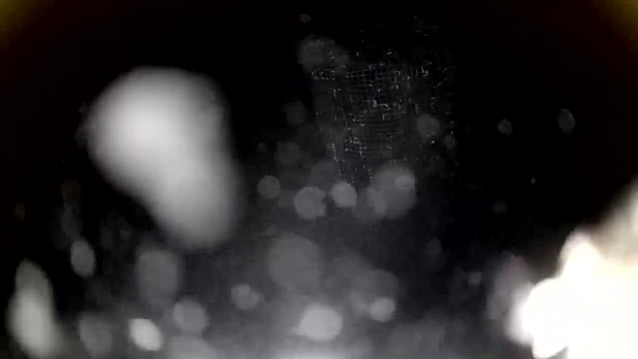 A blurry, out-of-focus image shows a dark, snowy scene with a wire mesh structure partially visible in the center.