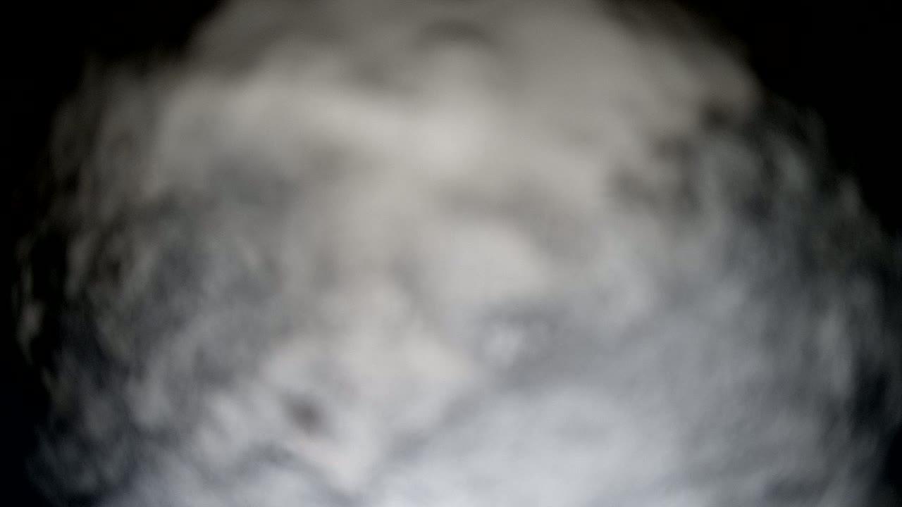 A blurry, out-of-focus image shows a swirling mass of gray and white smoke against a black background.