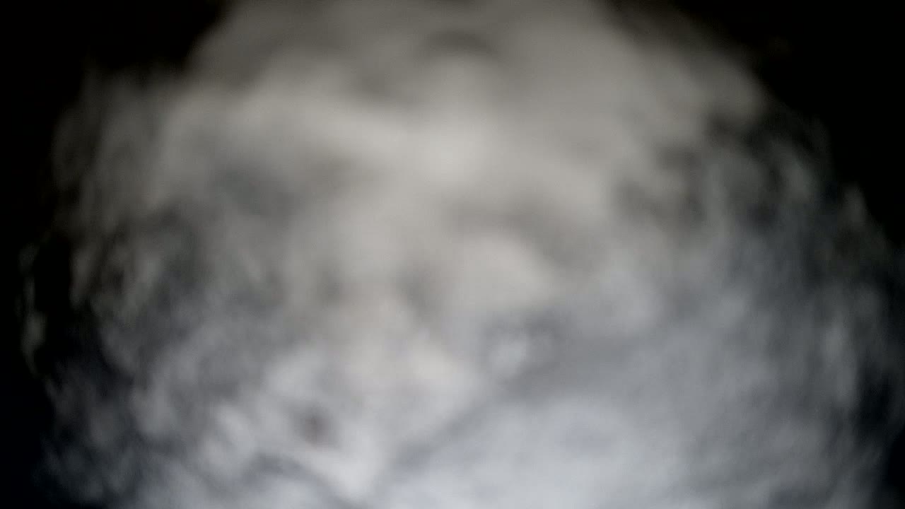 A blurry image shows a mass of gray and white smoke or fog against a black background.