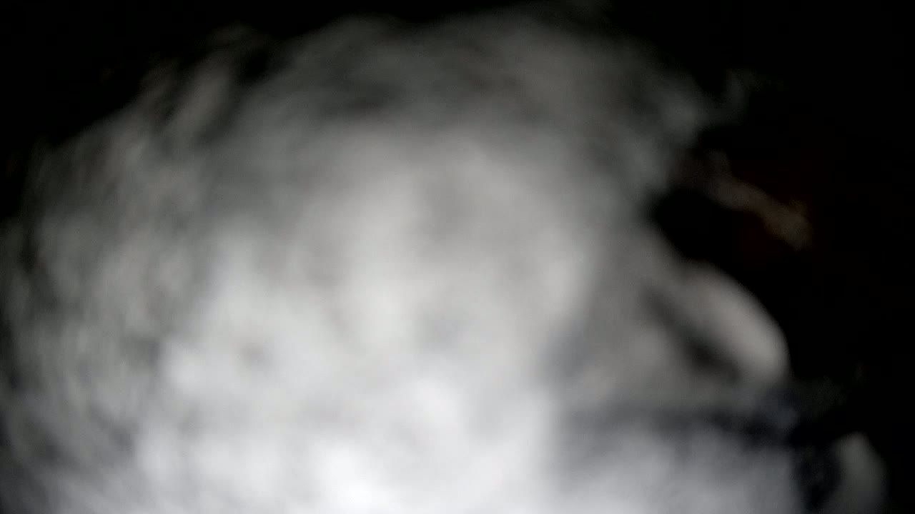 A blurry, out-of-focus image shows a mass of grey and white smoke or fog against a dark background.