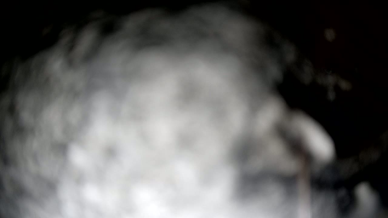 A blurry, out-of-focus image shows a large mass of gray and white smoke or fog against a dark background.