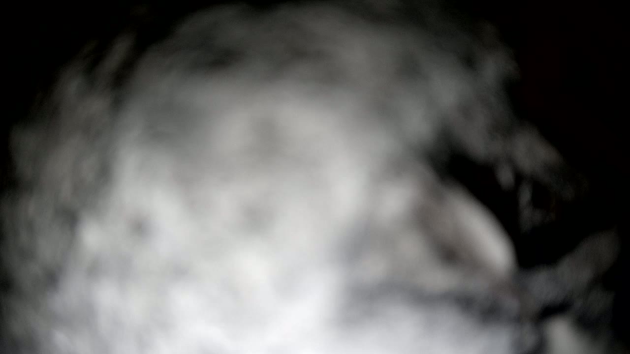 A blurry, out-of-focus image shows a mass of gray and white smoke or fog against a dark background.