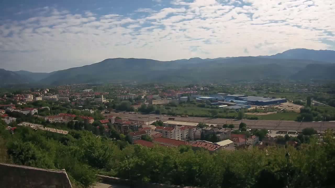 A sprawling town nestled in a valley between mountains under a partly cloudy sky.