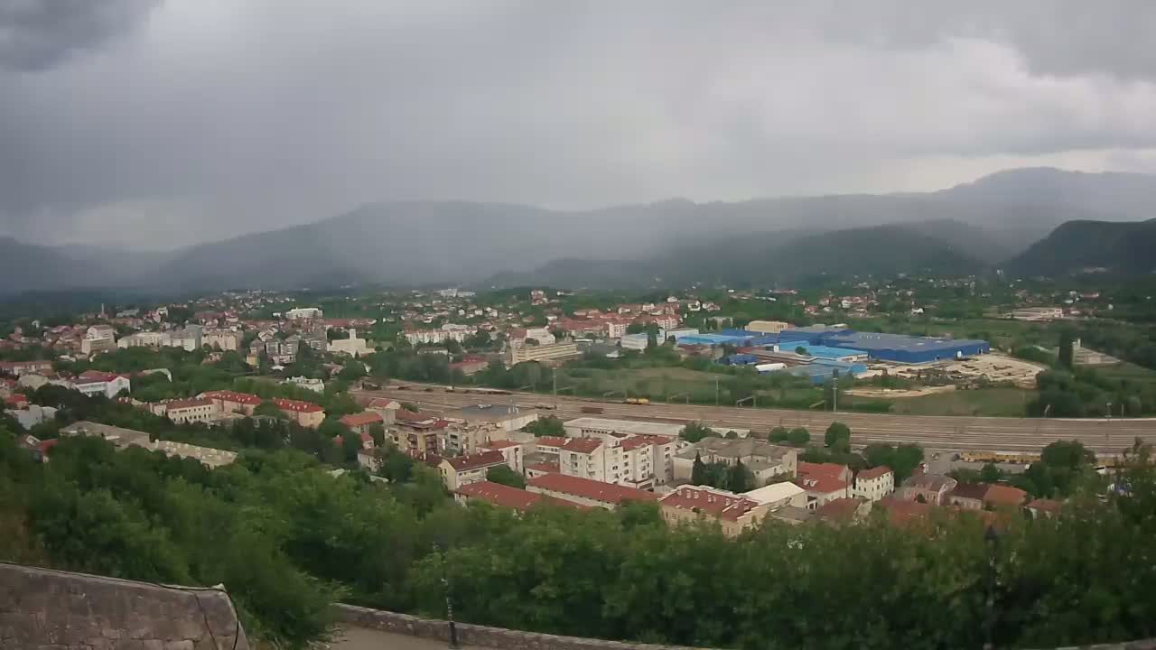 An overcast day reveals a sprawling town nestled in a valley, bordered by mountains and a railway line running through it.