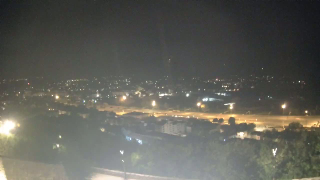 A nighttime, high-angle view shows a city illuminated by streetlights, with a highway visible in the middle ground.