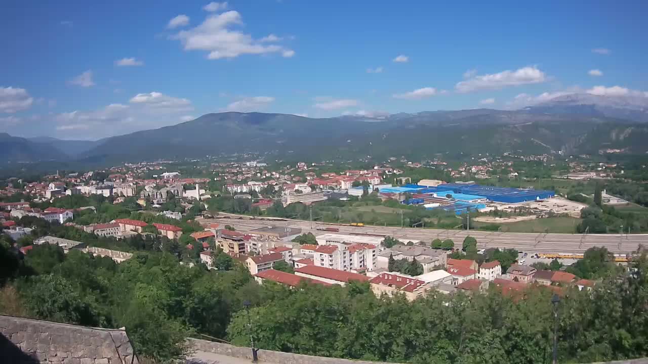 A sprawling town nestled in a valley between mountains under a mostly sunny sky with scattered clouds.