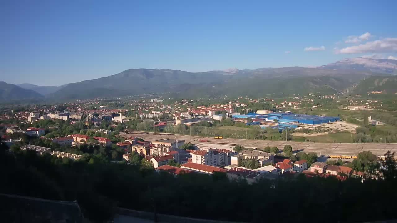 A sprawling town nestled in a valley between mountains under a clear, sunny sky.