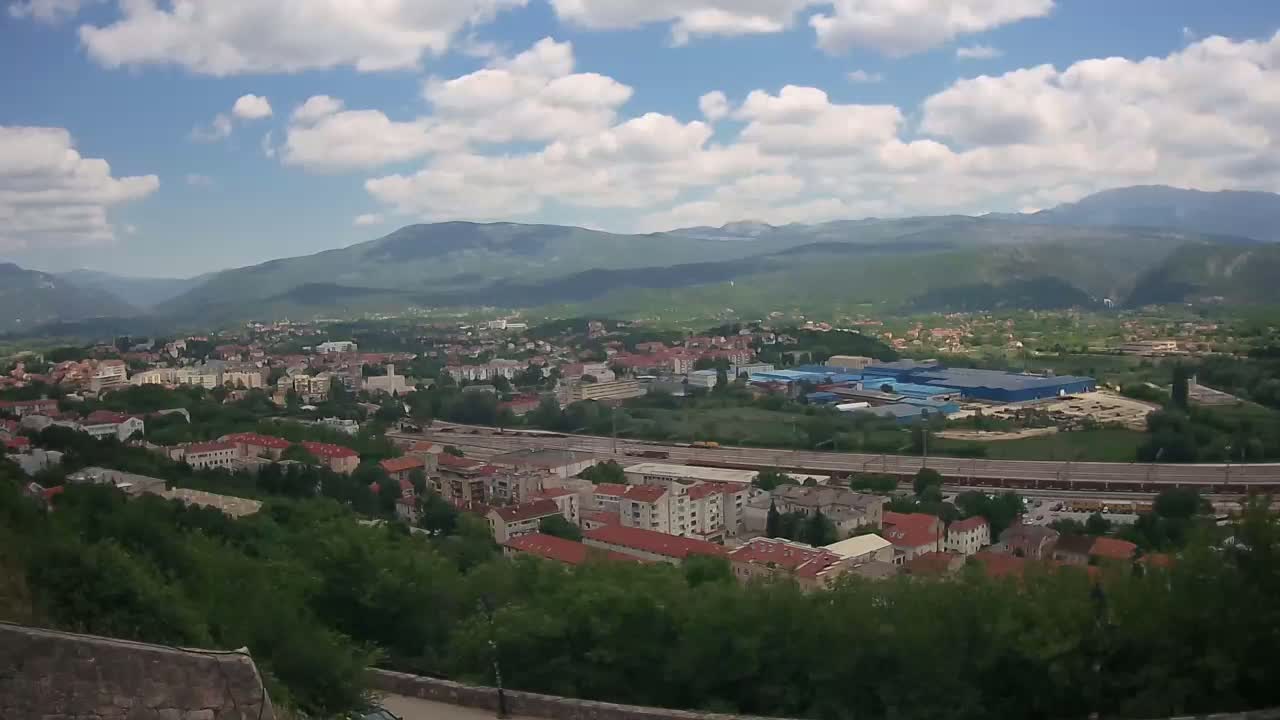 A sprawling town nestled in a valley, backed by mountains under a partly cloudy sky.