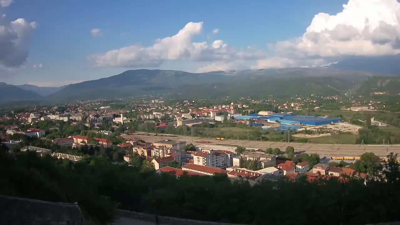A sprawling town nestled in a valley between mountains under a partly cloudy sky.