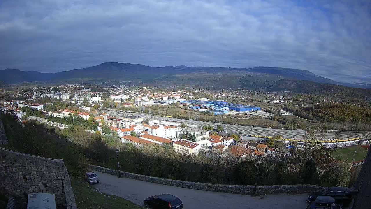 A sprawling town nestled in a valley between mountains under a partly cloudy sky.