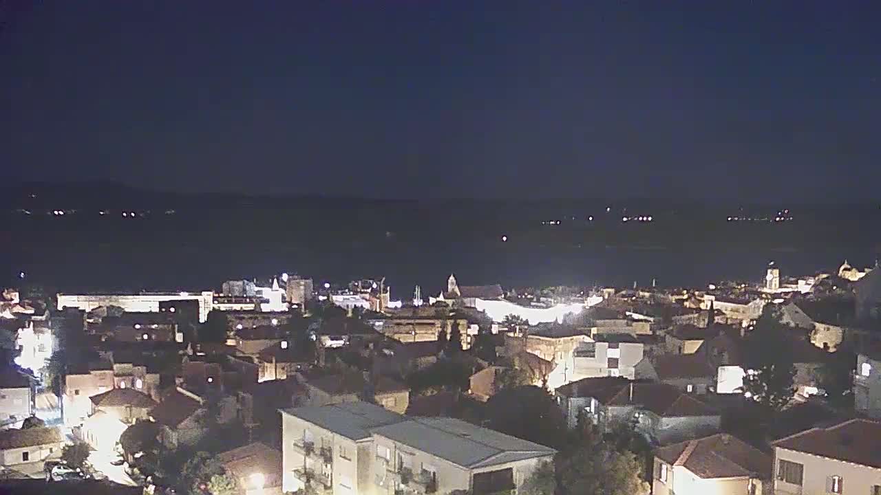 A nighttime view of a town illuminated by streetlights, overlooking a dark body of water under a clear, dark sky.