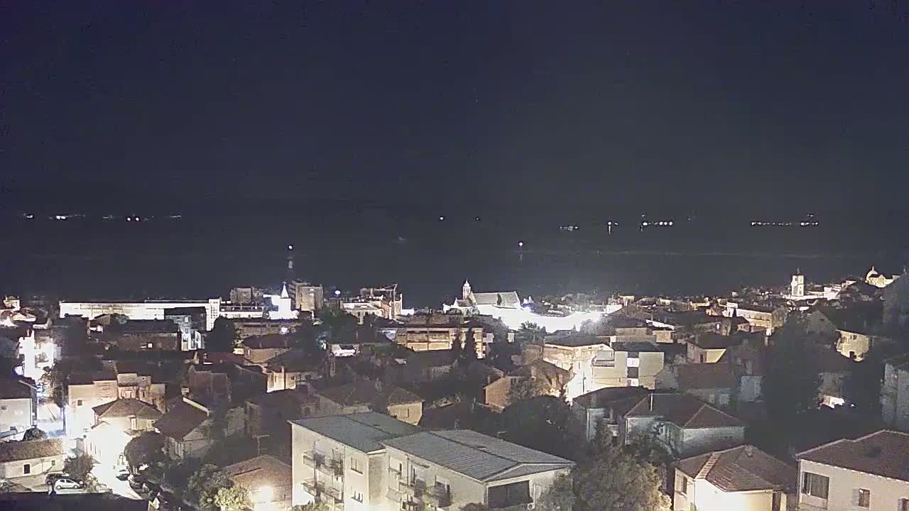 A nighttime view of a coastal town, illuminated by streetlights, overlooks a dark body of water.