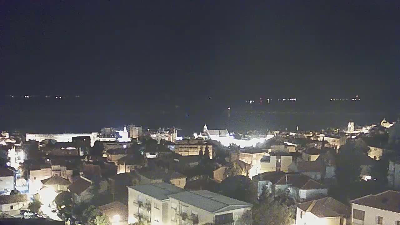 A nighttime, aerial view of a coastal town illuminated with streetlights, overlooking a dark body of water.
